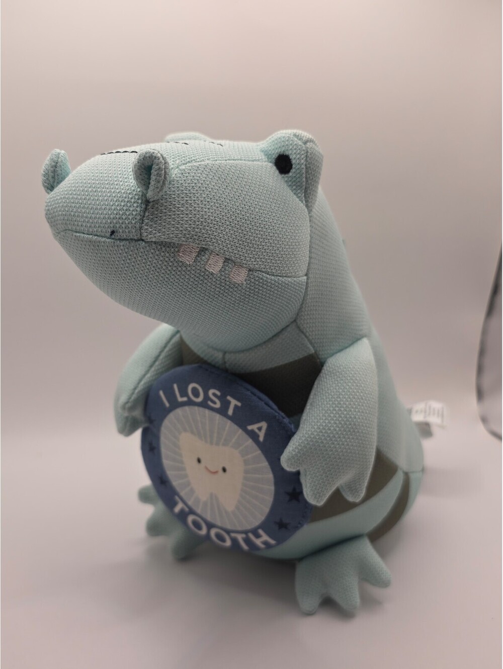 Pillowfort plush milestone alligator/dinosaur holding an “I lost a tooth” badge.